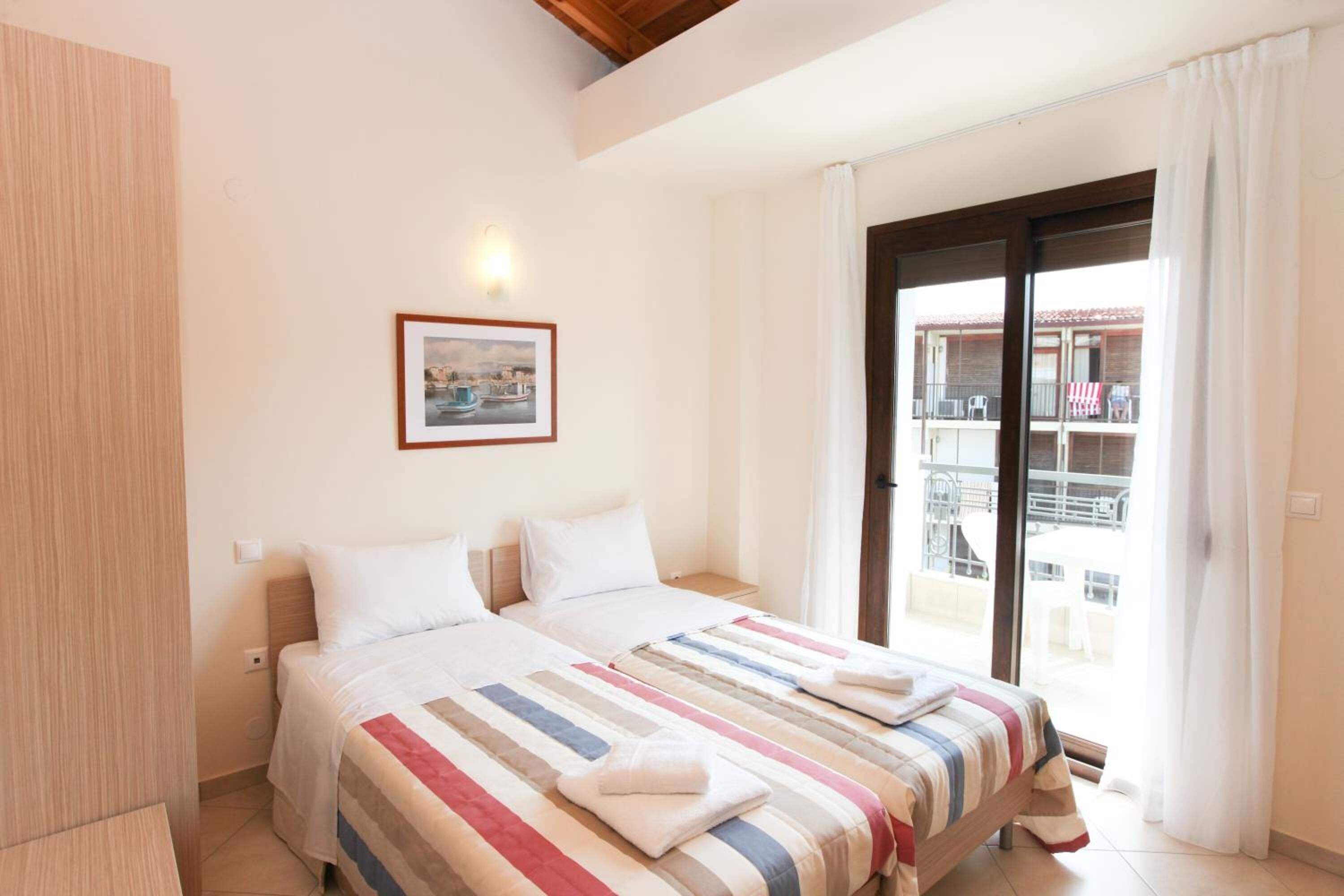 Une chambre d’hôtel avec deux lits, une grande fenêtre et un balcon aménagé avec du mobilier d’extérieur.