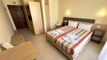 Quarto de hotel com cama, mesas de cabeceira, uma cadeira e uma escrivaninha.