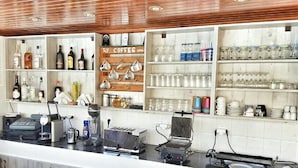 A bar area with shelves of liquor bottles, glasses, and a coffee machine. - Blue bay Hotel (Karpathos)