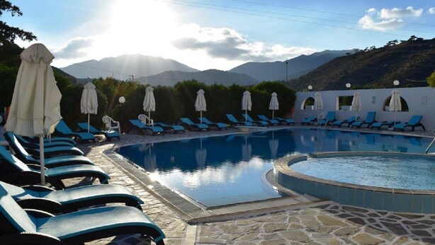 A pool area with lounge chairs and umbrellas, surrounded by mountains. - Blue bay Hotel (Karpathos)