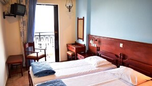 A hotel room with two beds, a desk, a chair, and a balcony with a railing. - Blue bay Hotel (Karpathos)
