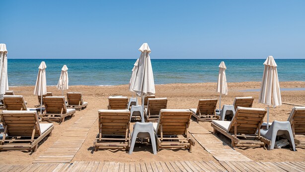 Une plage avec des chaises longues en bois et des parasols blancs disposés sur une terrasse en bois.