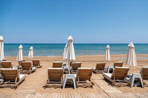 Una playa con sillones de madera y sombrillas blancas dispuestas sobre una terraza de madera.