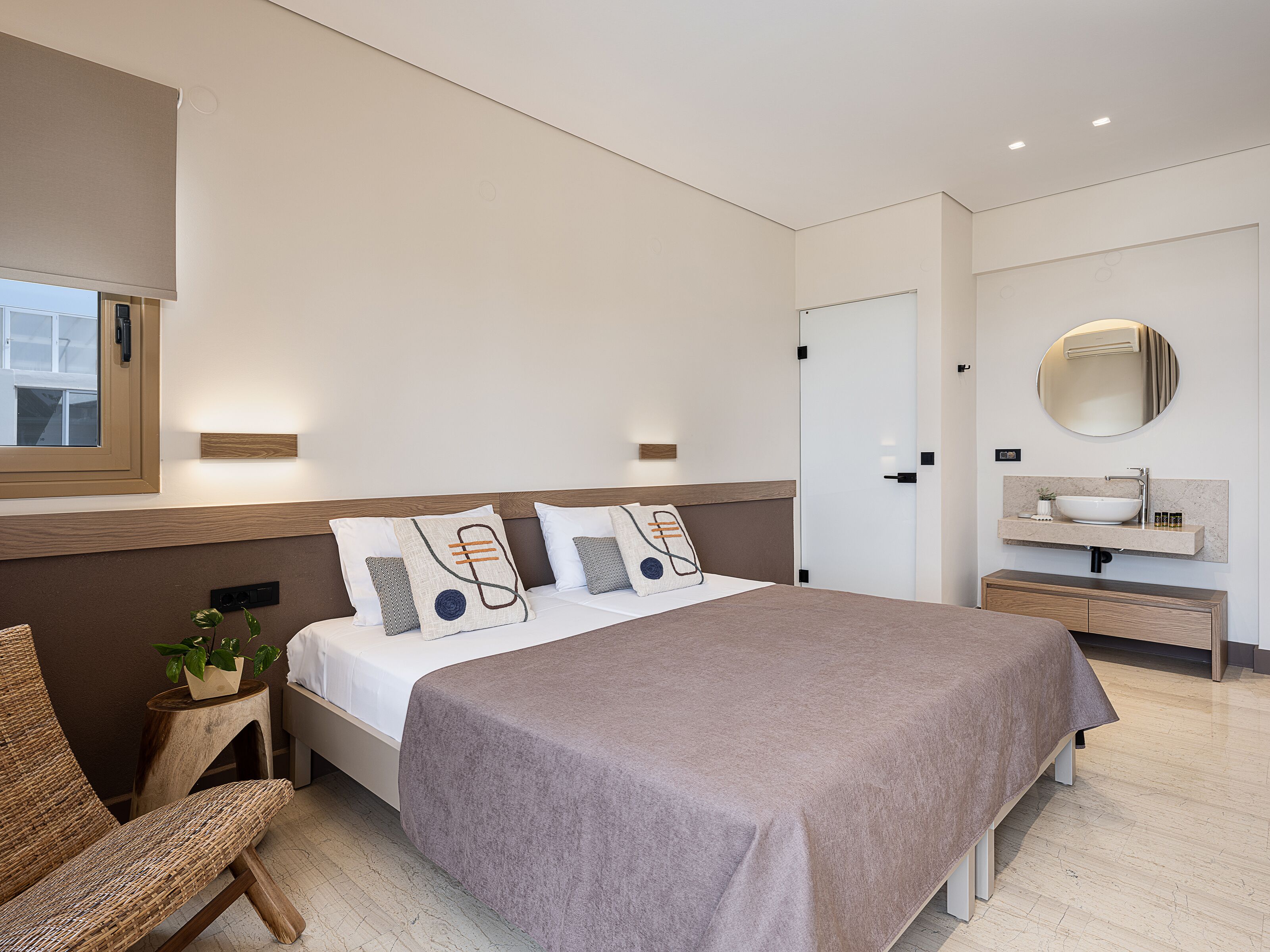 A modern bedroom with a large bed, bedside tables, a round mirror, and a window.
