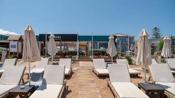 A beachside resort with sun loungers, umbrellas, and a wooden walkway leading to the beach.