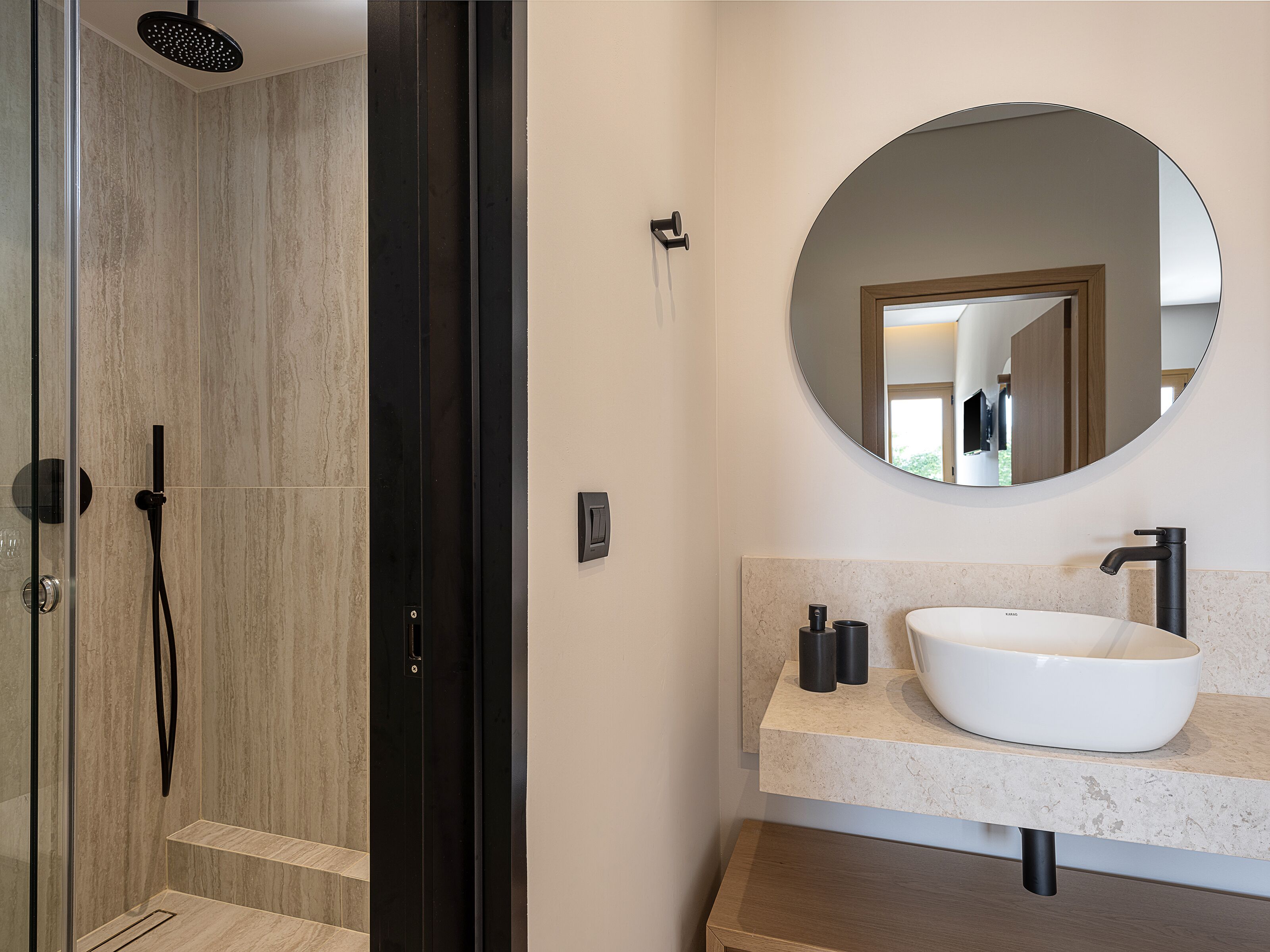 A modern bathroom with a glass-enclosed shower, a round mirror, and a white sink with a marble countertop.