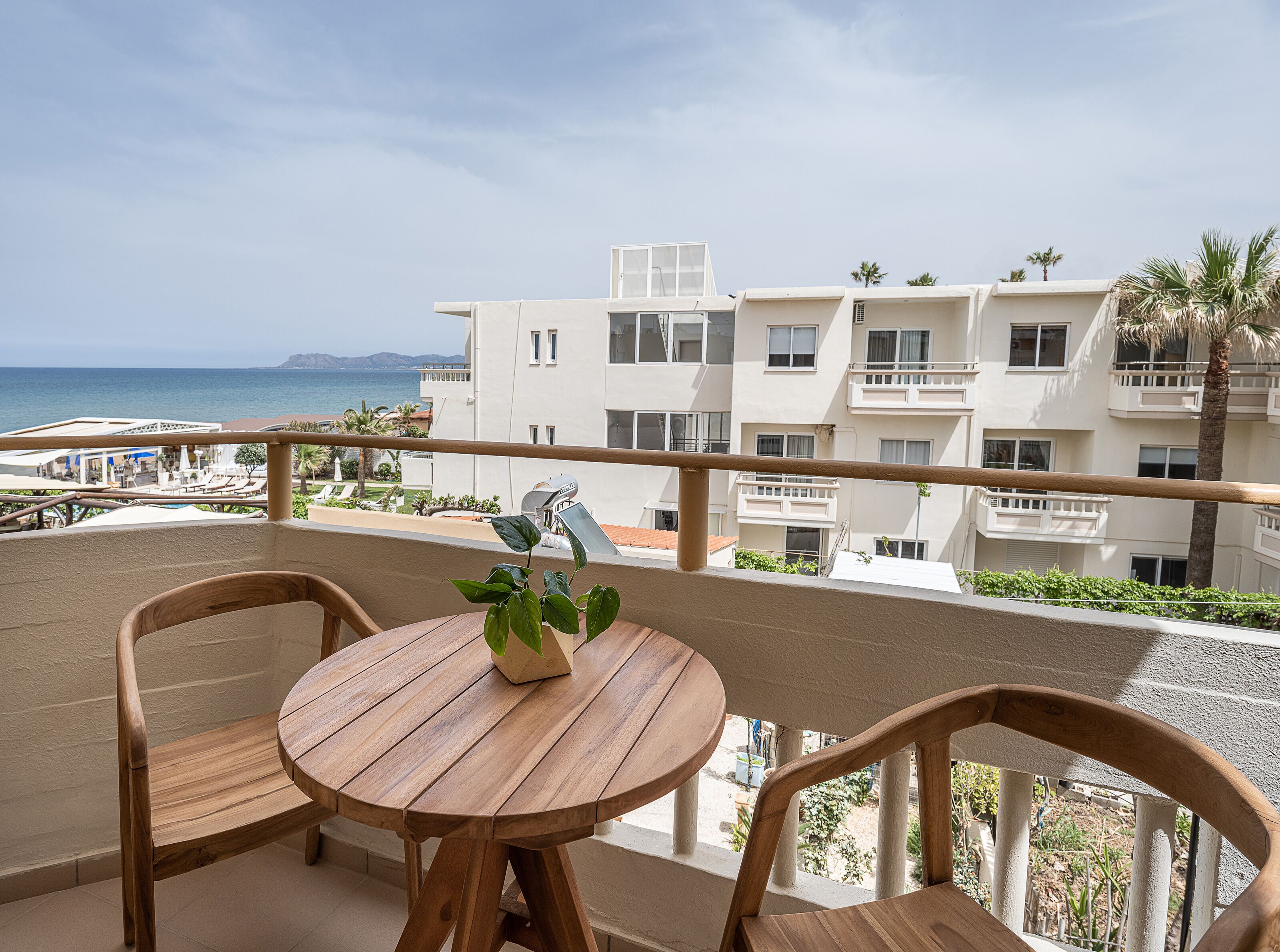 Un balcón con sillas y una mesa de madera, con vista a una piscina y un edificio con balcones.