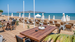 Un restaurant situé en bord de mer, avec une terrasse comprenant des tables, des chaises et des parasols pour offrir de l’ombre.