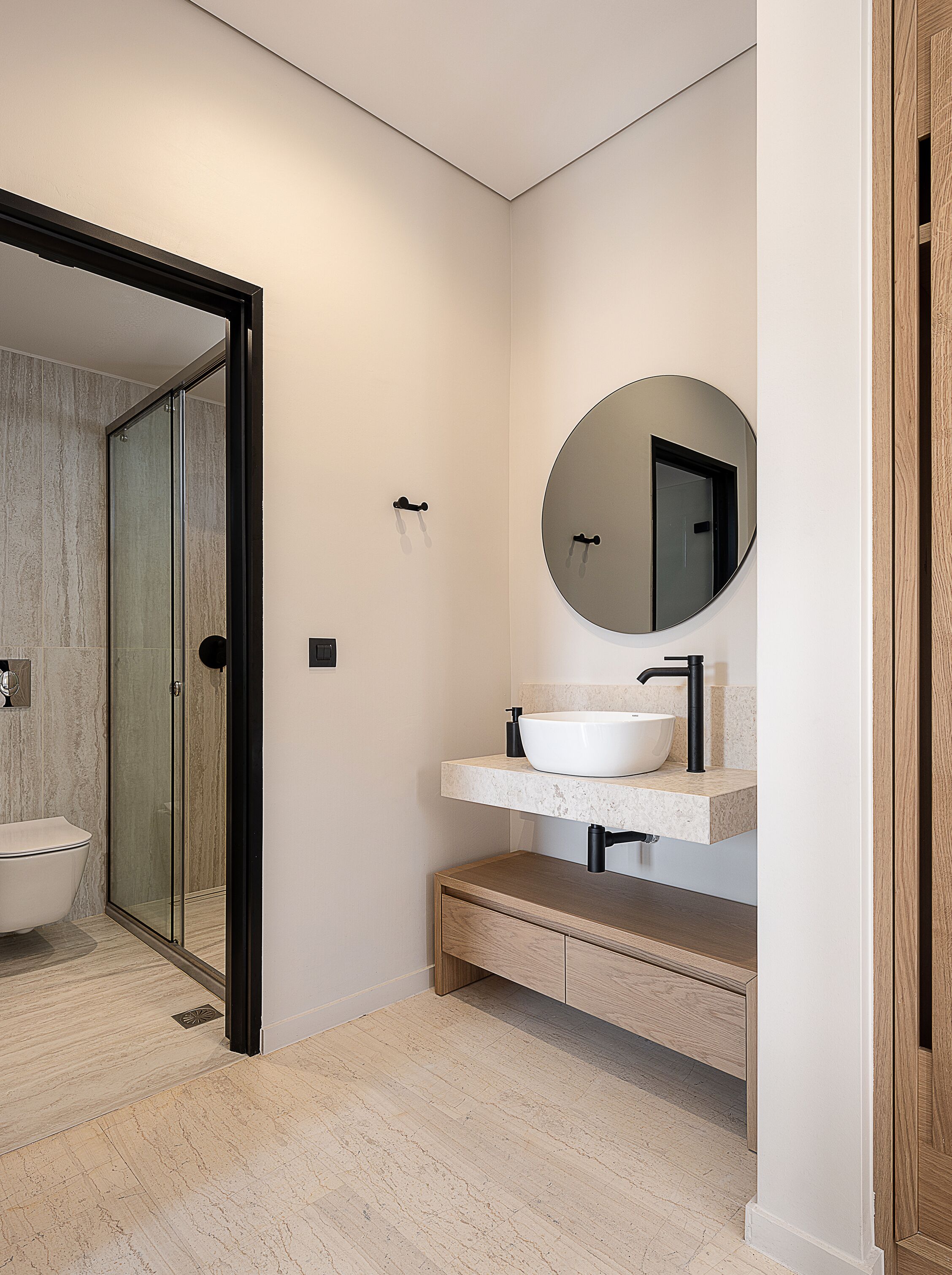 Un baño moderno con cabina de ducha de vidrio, una bañera independiente, un lavabo tipo cuenca blanco y un mueble de tocador de madera.