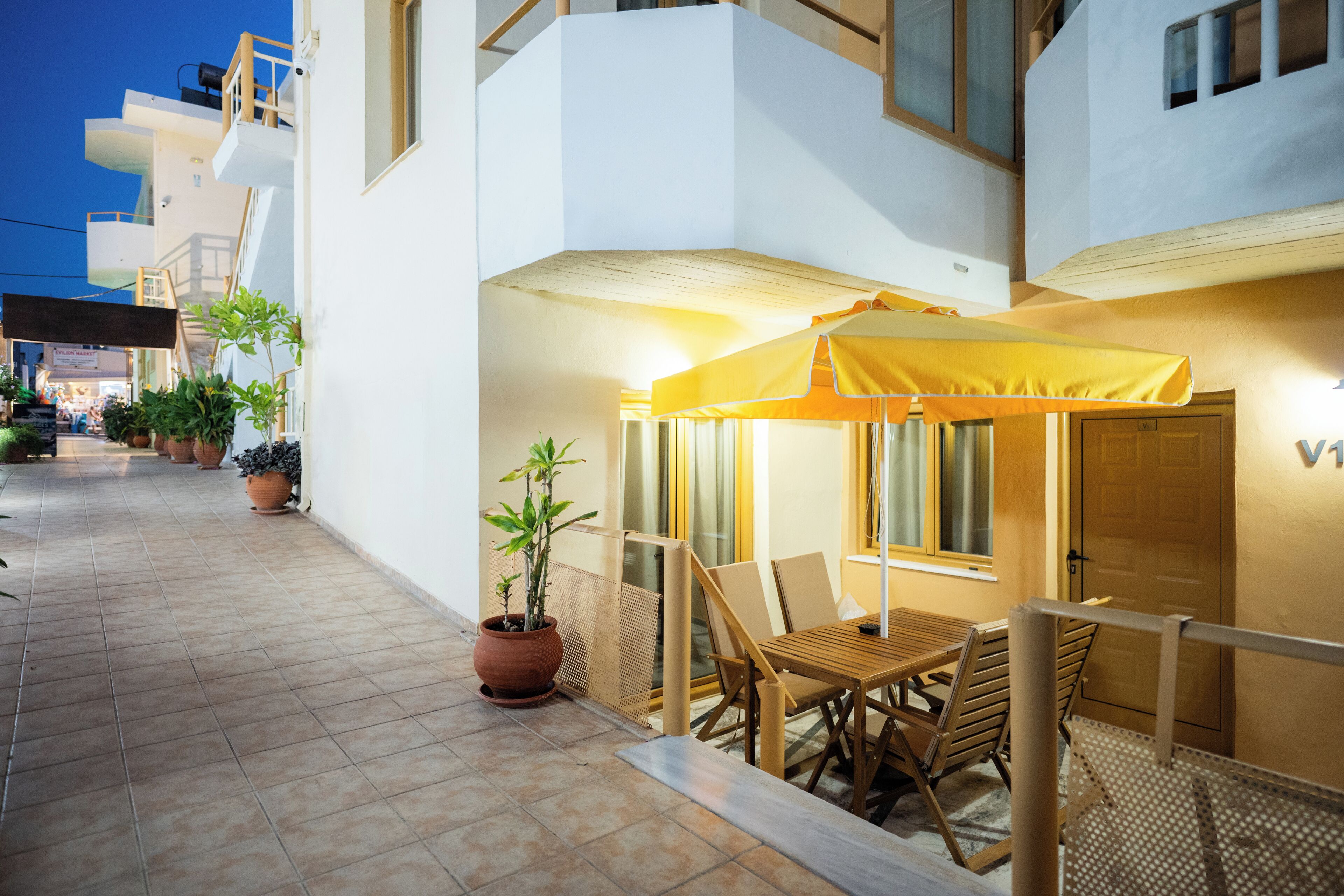 Eine Terrasse mit Tisch und Stühlen, Topfpflanzen und einem gelben Sonnenschirm.
