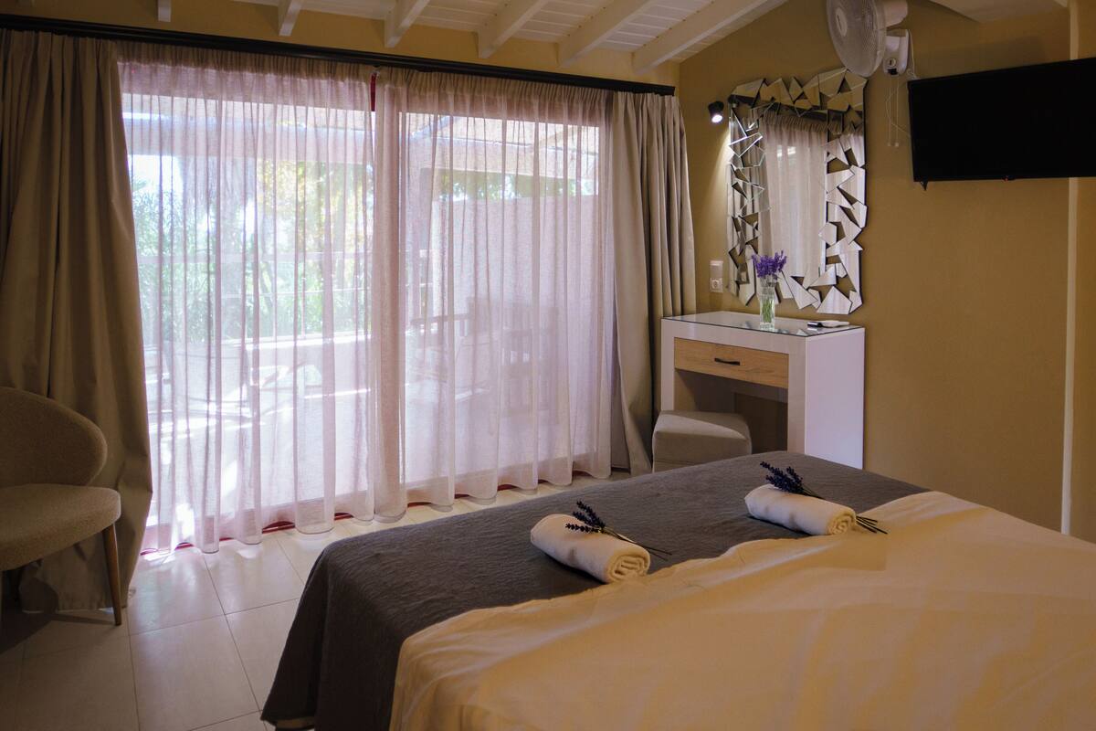 A hotel room with a bed, a desk, a chair, a mirror, and a window with curtains.