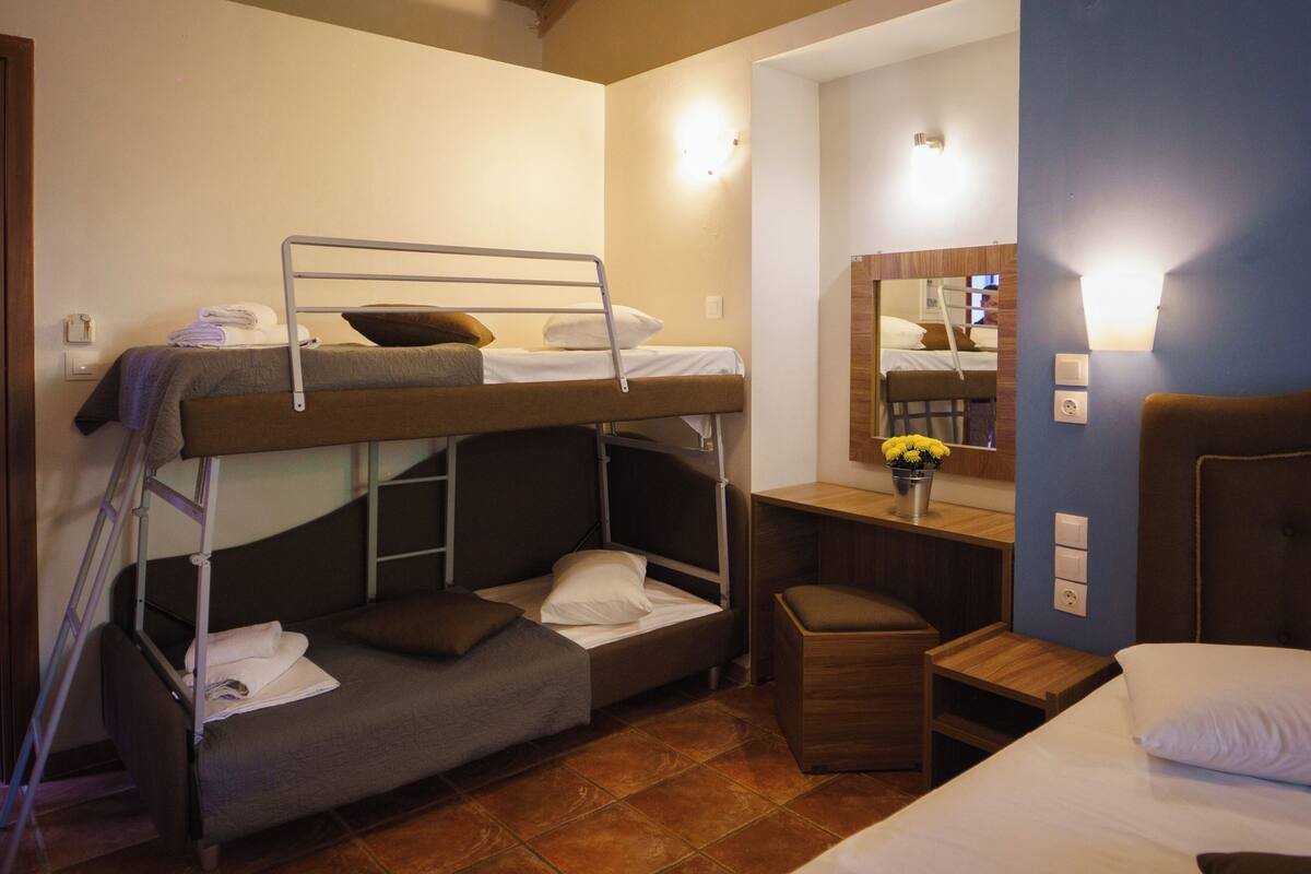 A bunk bed room with a desk, chair, and a small stool.