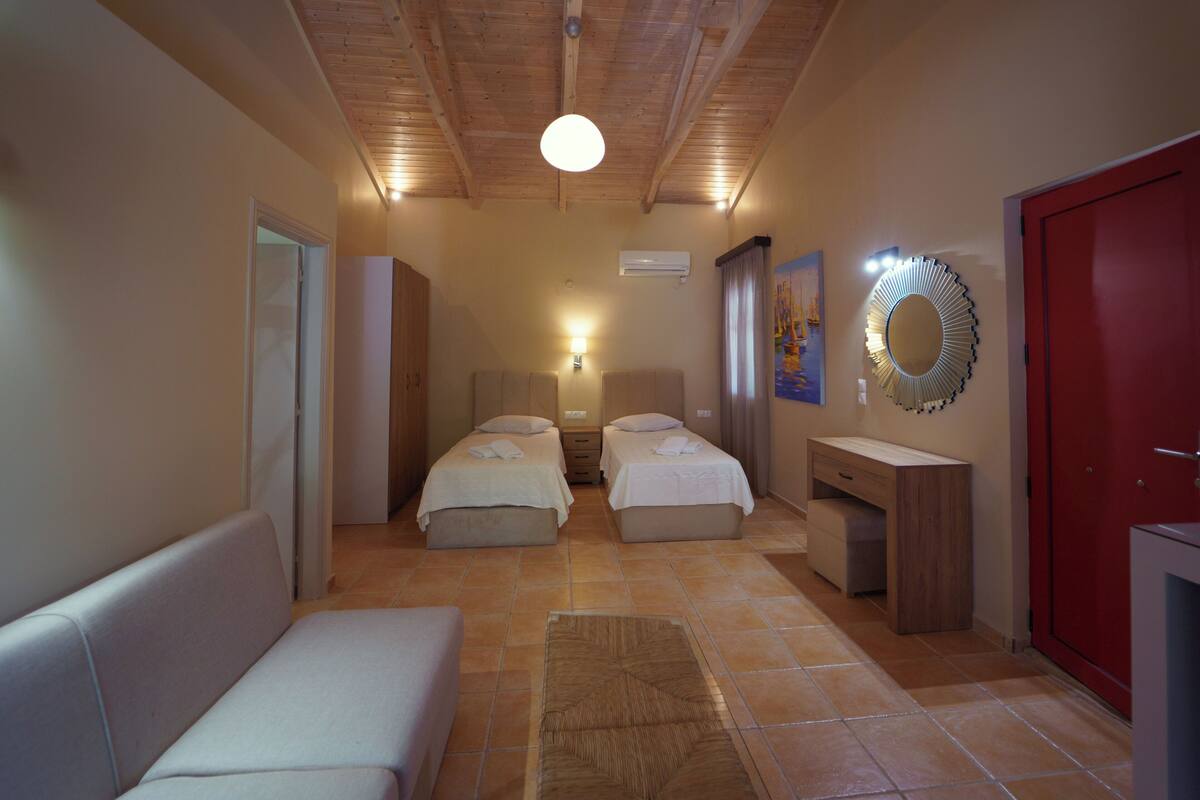 A hotel room with two beds, a small desk, a mirror, and a red door.