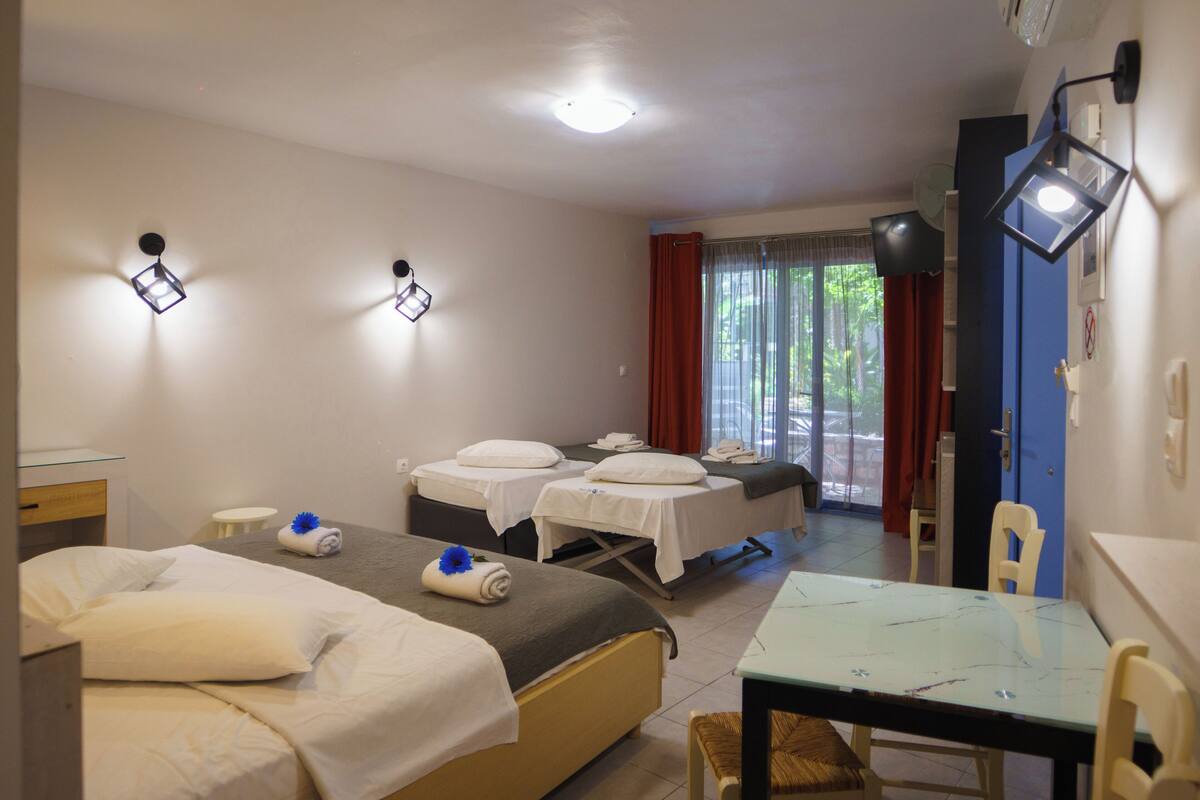 A hotel room with two beds, a small table, and a chair. There are wall-mounted lights and a ceiling fan.