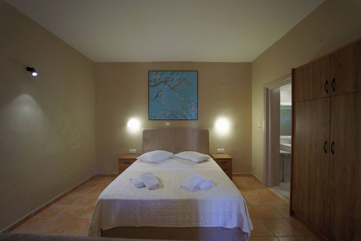 A hotel room with a bed, two bedside tables, a nightstand, a wardrobe, and a painting on the wall.