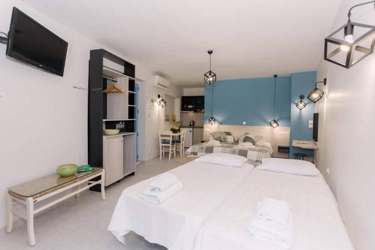A hotel room with a bed, a desk, a chair, a TV, and a kitchenette.