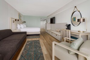 Une chambre d’hôtel comprenant un lit, un canapé, un bureau avec une chaise, une télévision et un miroir.
