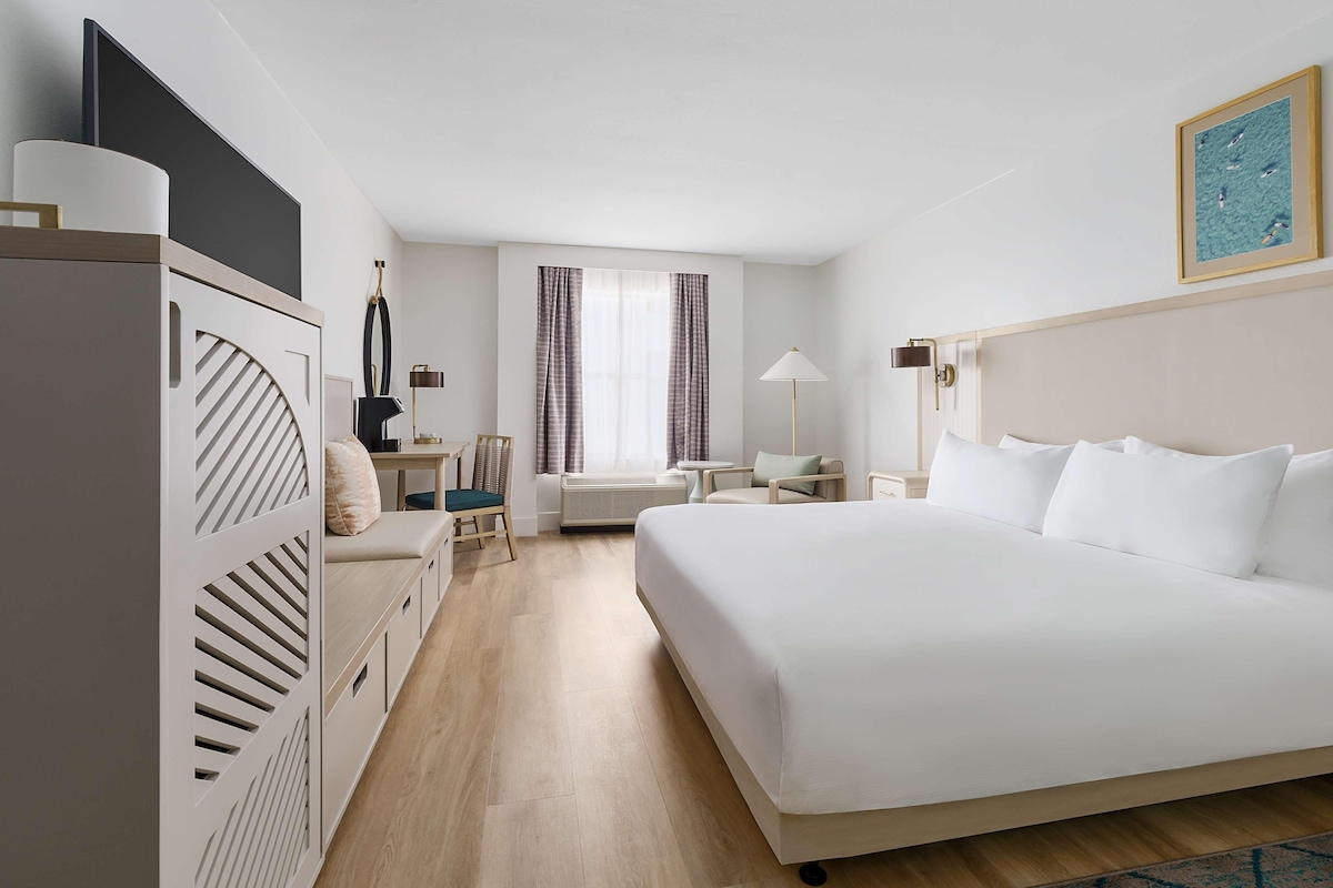 Una camera d'albergo con un letto grande, una scrivania con una sedia, un tavolino e una finestra con tende.