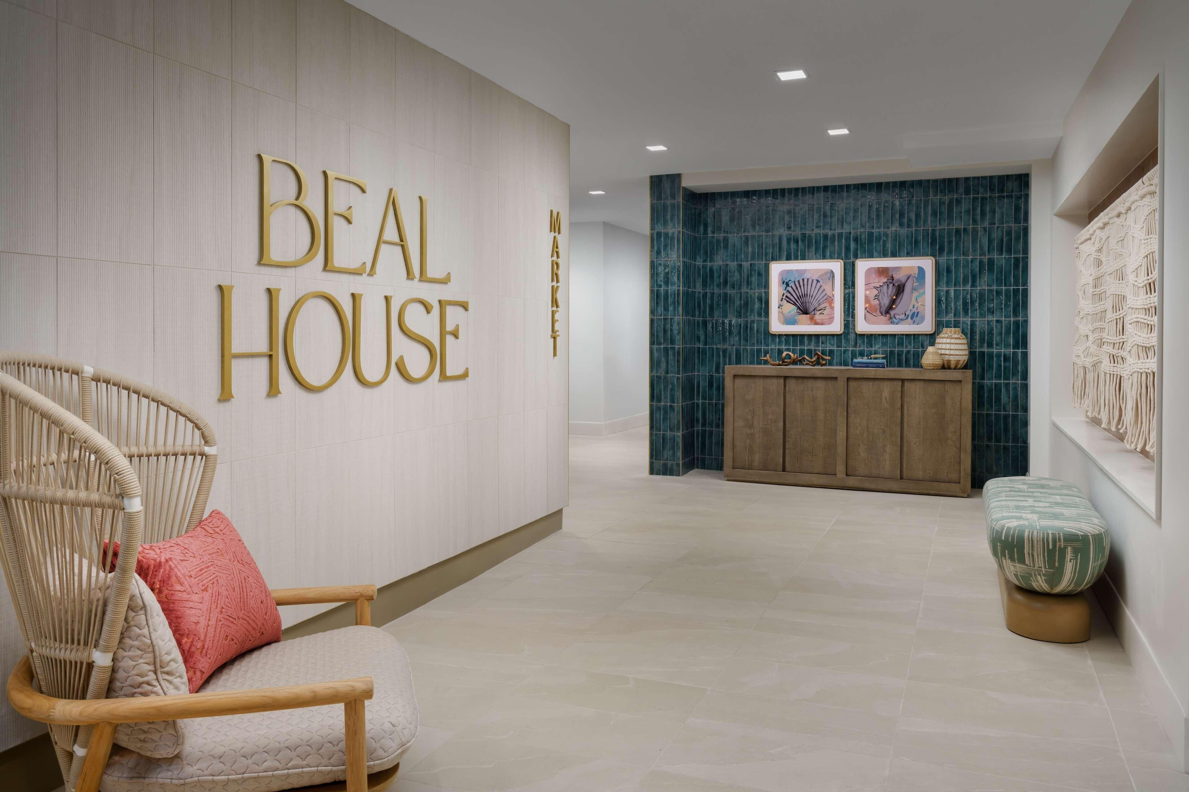 Um hall de entrada com uma placa 'BEAL HOUSE', uma cadeira de madeira com almofadas, um armário de madeira com objetos decorativos e uma parede com azulejos azuis.