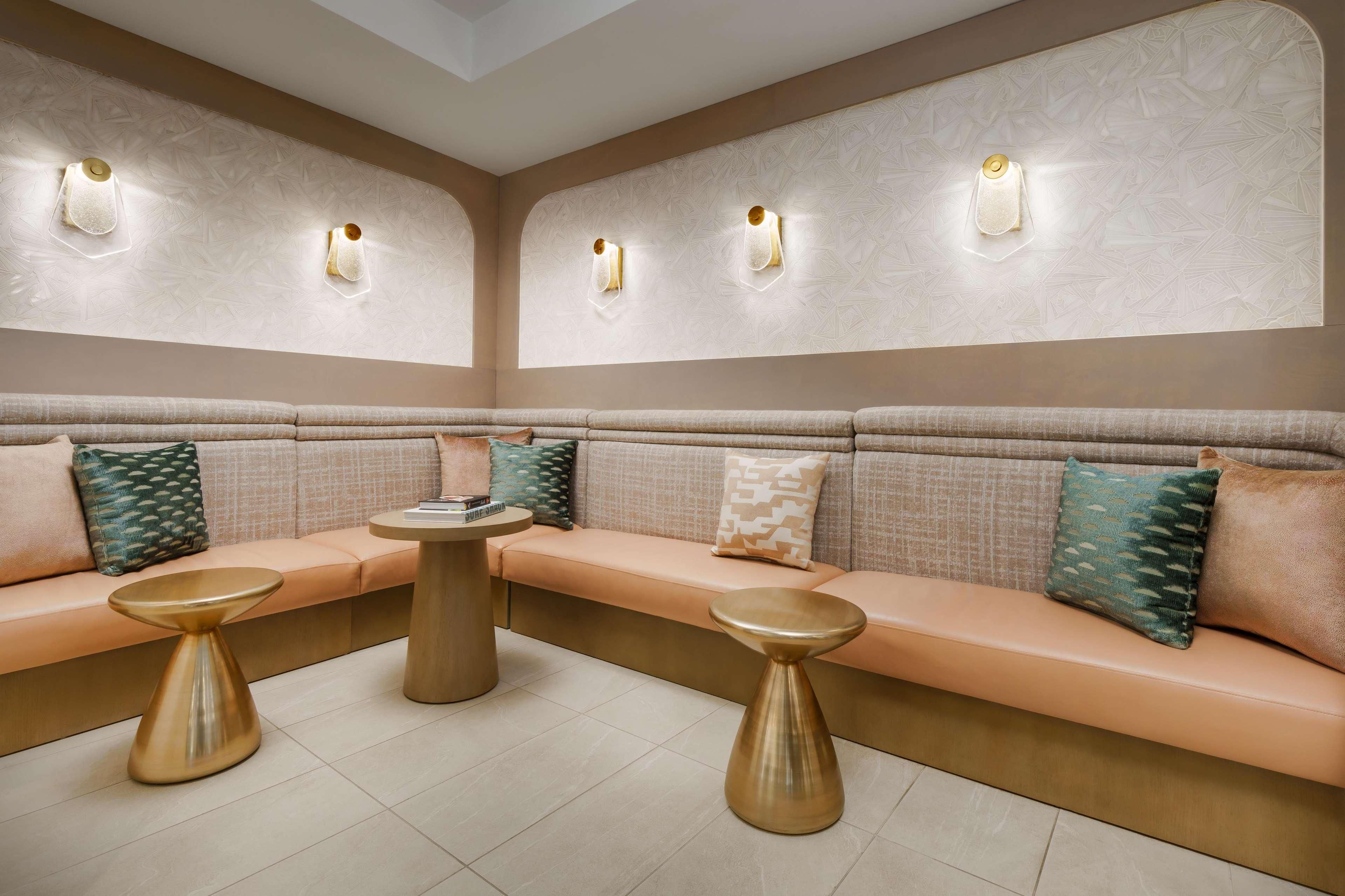 A modern lounge area with a beige sofa set, two gold-toned side tables, and wall-mounted lighting fixtures.