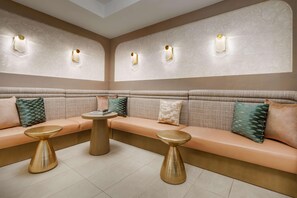 A modern lounge area with a beige sofa set, two gold-toned side tables, and wall-mounted lighting fixtures. - Bealhousefort Walton Beachfront Tapestrycollection (Fort Walton Beach)