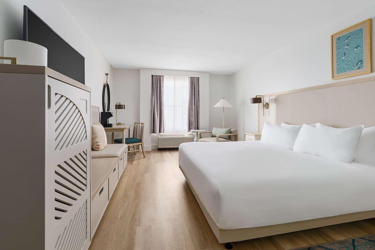 Een hotelkamer met een groot bed, een bureau met een stoel, een klein tafeltje en een raam met gordijnen.