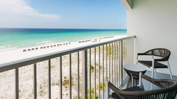Un balcon meublé avec des meubles en osier, donnant sur une plage parsemée de parasols.