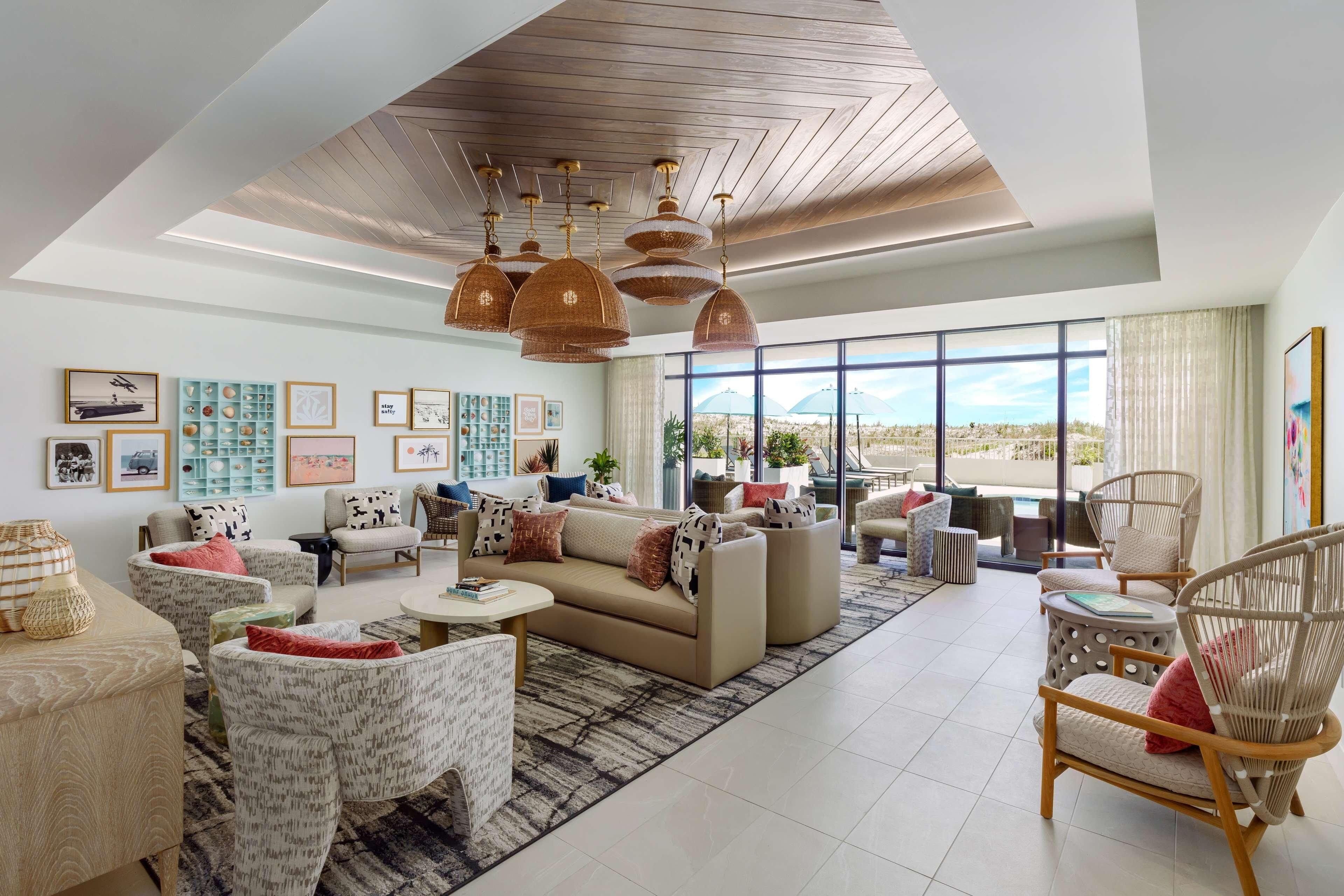 Un vaste salon doté d’un haut plafond, de grandes fenêtres et d’une vue sur le désert. Le mobilier comprend un canapé beige, des fauteuils à motifs et un fauteuil en osier.