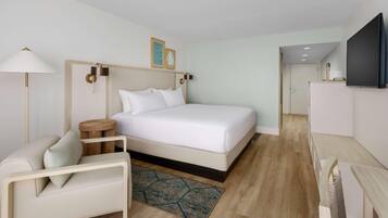 A modern hotel room with a large bed, a desk, a television, and a small side table.