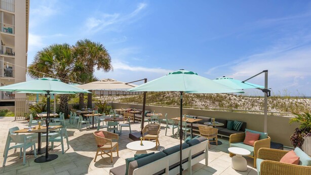 Un espace extérieur aménagé en terrasse, avec des tables, des chaises et des parasols, donnant sur une plage.