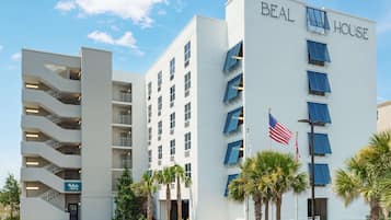 A multi-story hotel with a white facade, named "BEAL HOUSE," featuring a central entrance, multiple balconies, and an American flag.