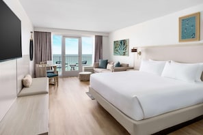 Habitación de hotel con una cama grande, un rincón de descanso con una mesa y sillas, y un balcón con vistas.
