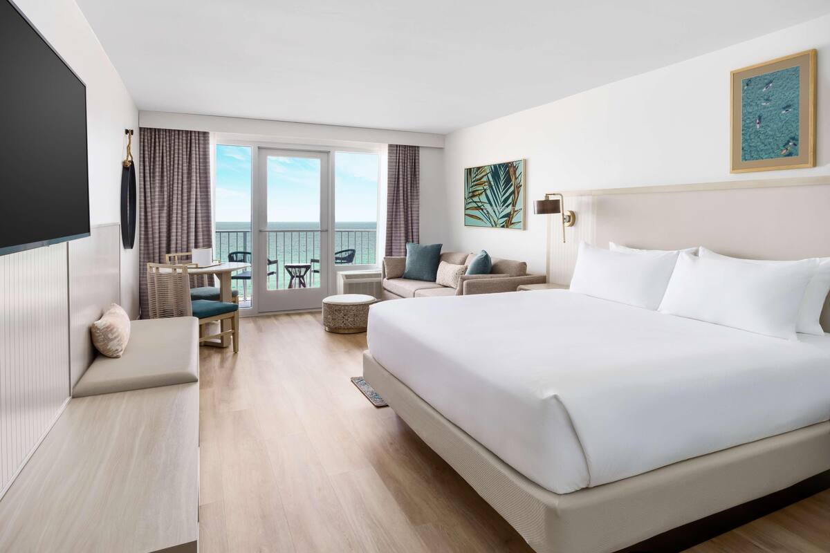 Een hotelkamer met een groot bed, een zithoek met een tafel en stoelen, en een balkon met uitzicht.