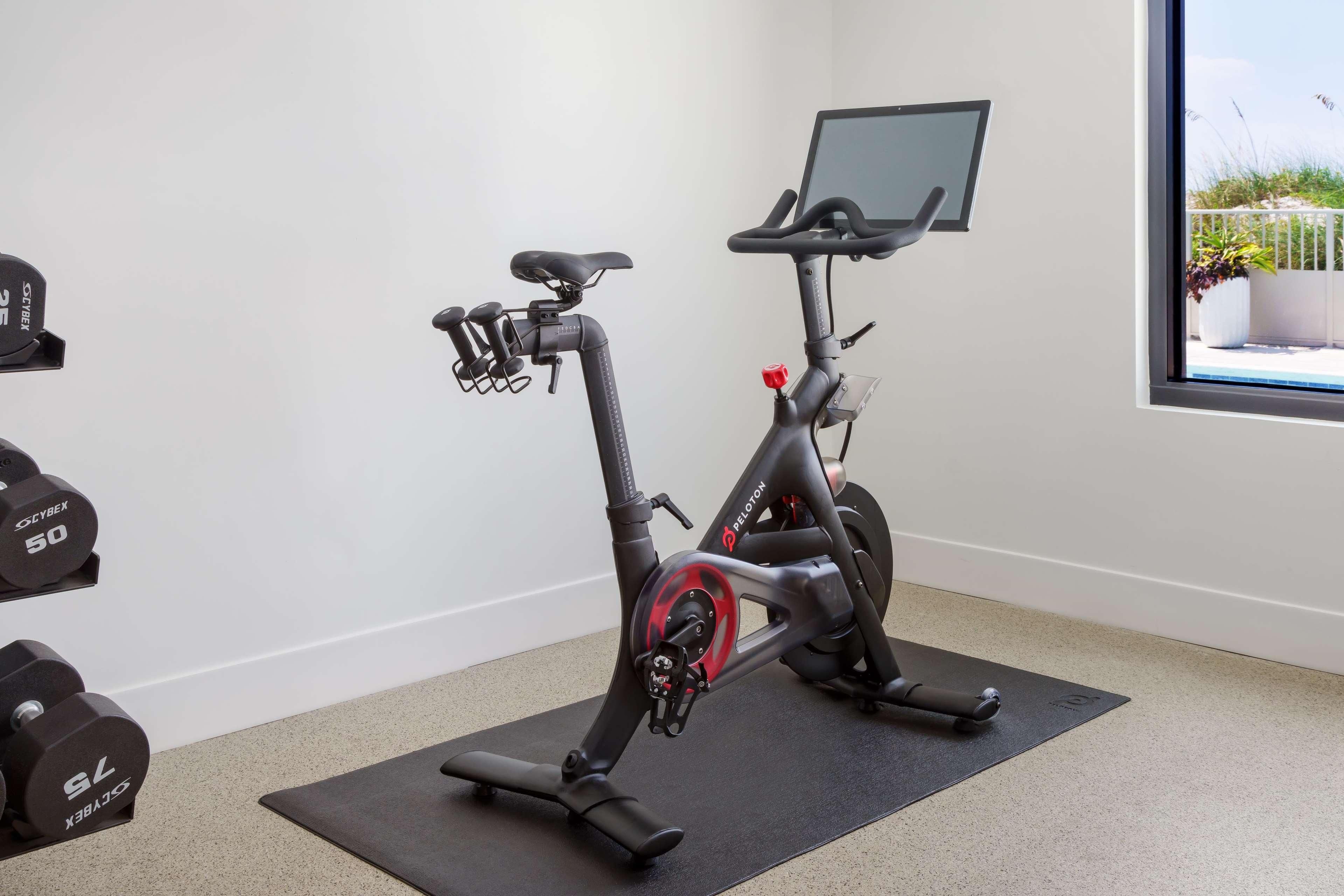 Uma bicicleta ergométrica com tela, dois halteres e uma janela com vista.