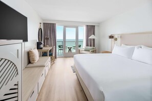 Habitación de hotel con una cama grande, un escritorio con silla, una mesita con sillas y un balcón con vista al mar.