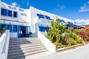 Um hotel de dois andares com fachada branca e detalhes em azul, apresentando um conjunto de degraus que levam à entrada.