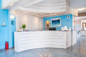 Un comptoir d’accueil au design incurvé, un mur bleu orné de motifs évoquant le thème maritime et un sol carrelé.