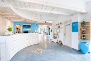 A hotel reception area with a curved reception desk, a blue wall with a seascape painting, and a reception desk with a computer.