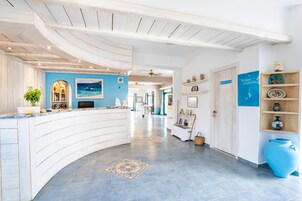 A hotel reception area with a curved reception desk, a blue wall with a seascape painting, and a reception desk with a computer.