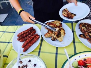 A table with plates of grilled food, a bowl of salad, and a glass of a white beverage with a straw.