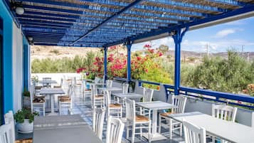 An outdoor patio with white tables and chairs, a blue ceiling, and a view of the landscape.