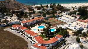 Eine Luftaufnahme eines Resorts mit mehreren Gebäuden, einem zentralen Poolbereich und einem Strand im Hintergrund.