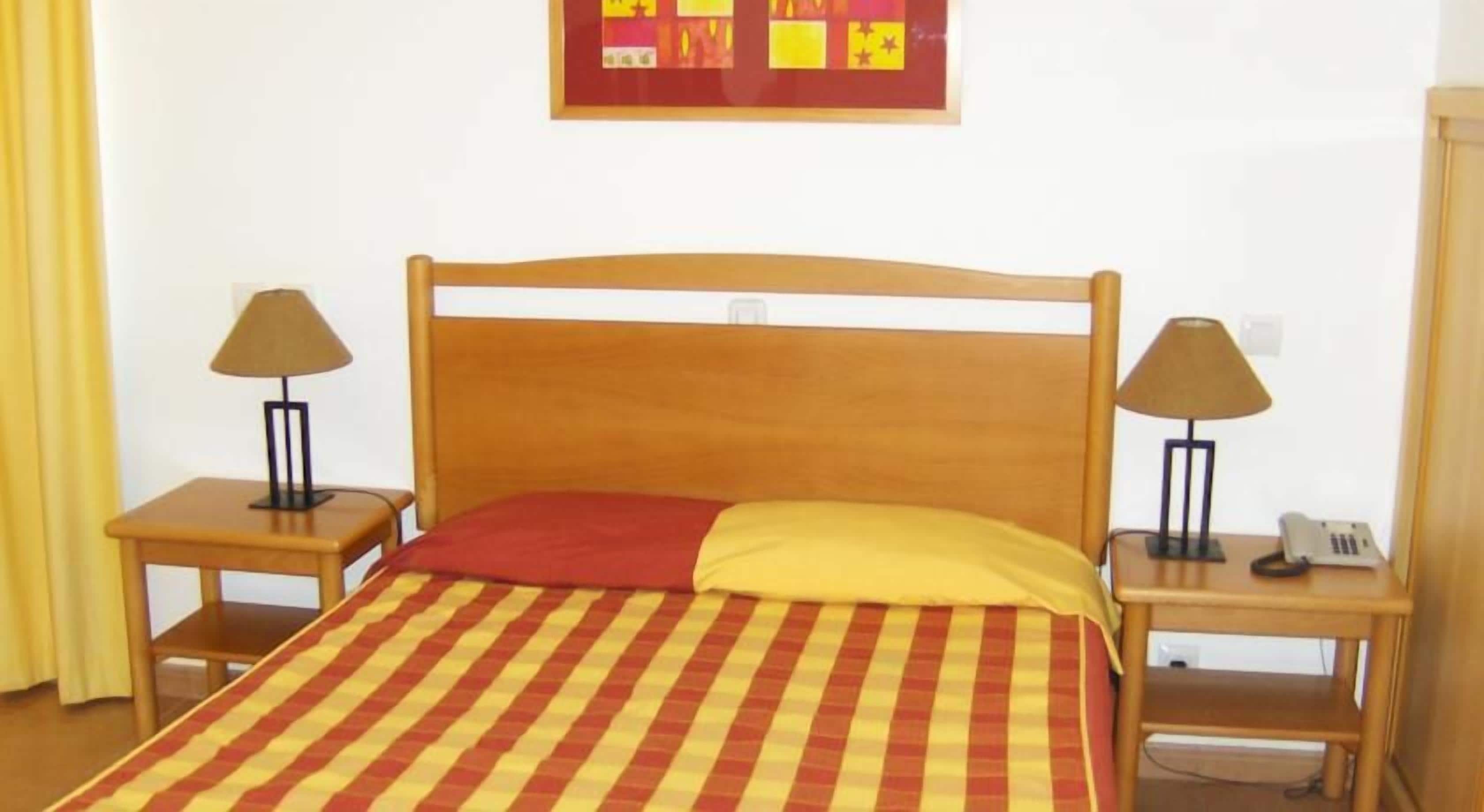 A single bed with a striped bedspread, two bedside tables with lamps, and a wall-mounted telephone.