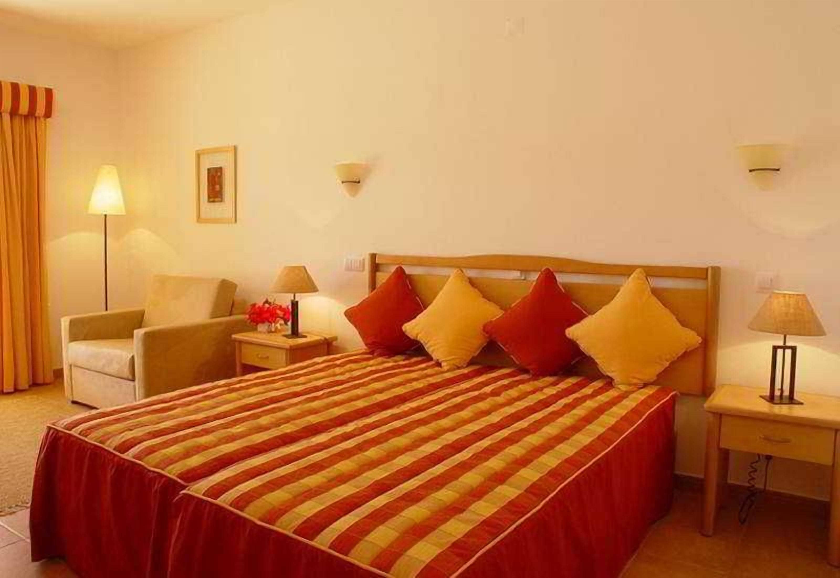 A hotel room with a large bed, a chair, a nightstand, and a lamp.