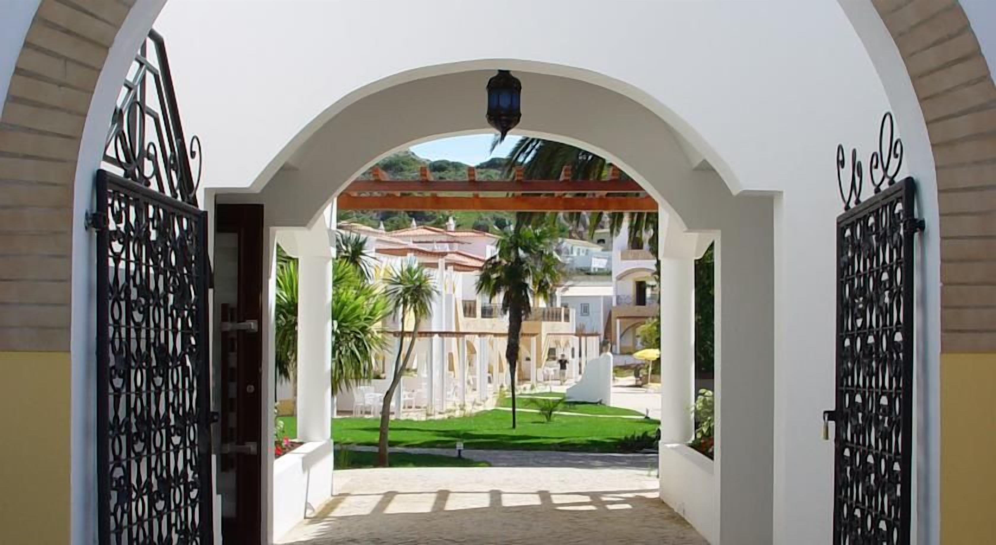 Uma entrada em arco com vista para um edifício e palmeiras.