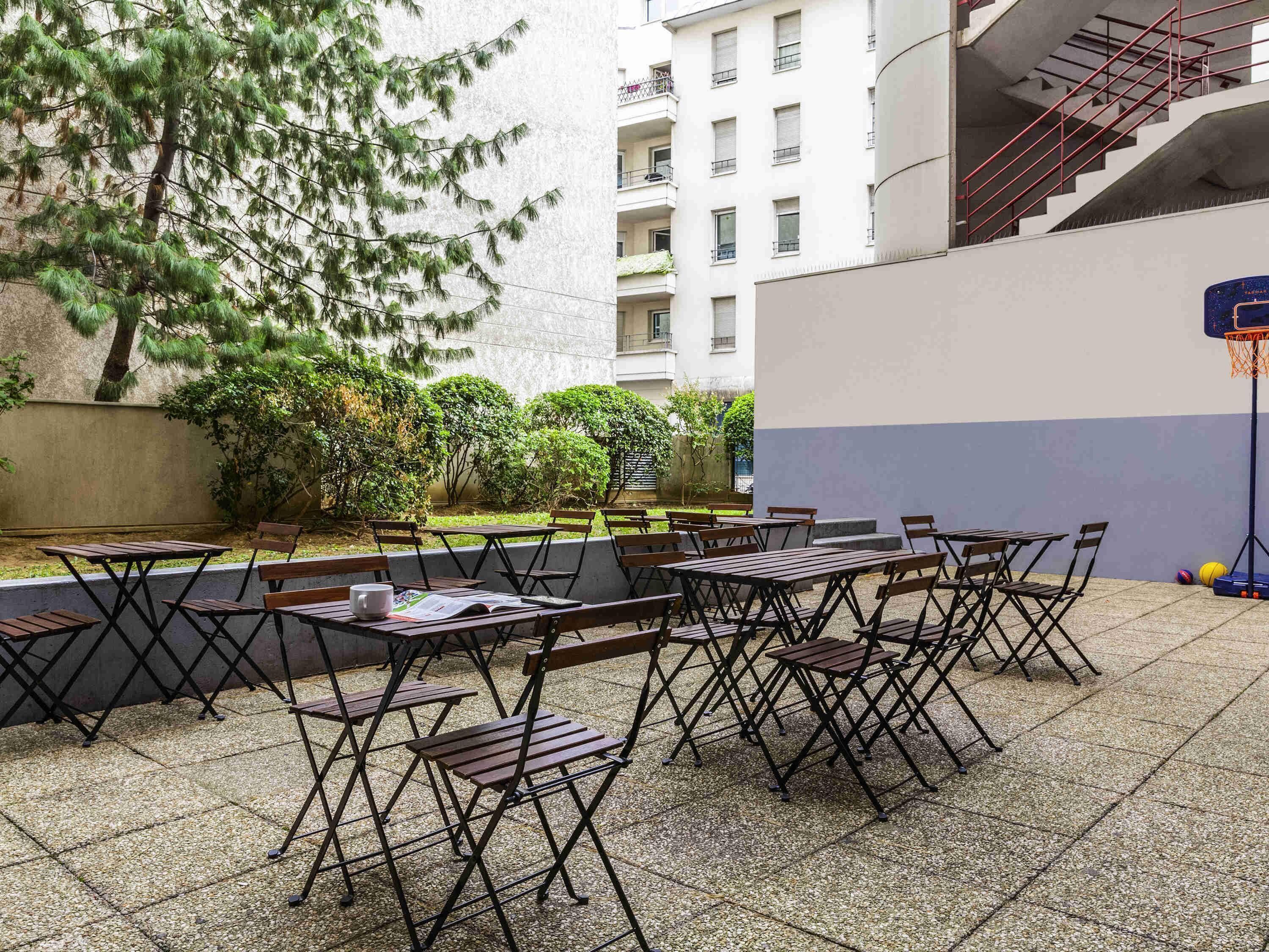 Un patio al aire libre con mesas y sillas plegables, un aro de baloncesto y un edificio al fondo.