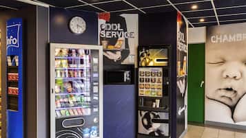 A vending machine area with a clock, a service sign, and a baby poster.