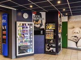 A vending machine area with a clock, a service sign, and a baby poster.