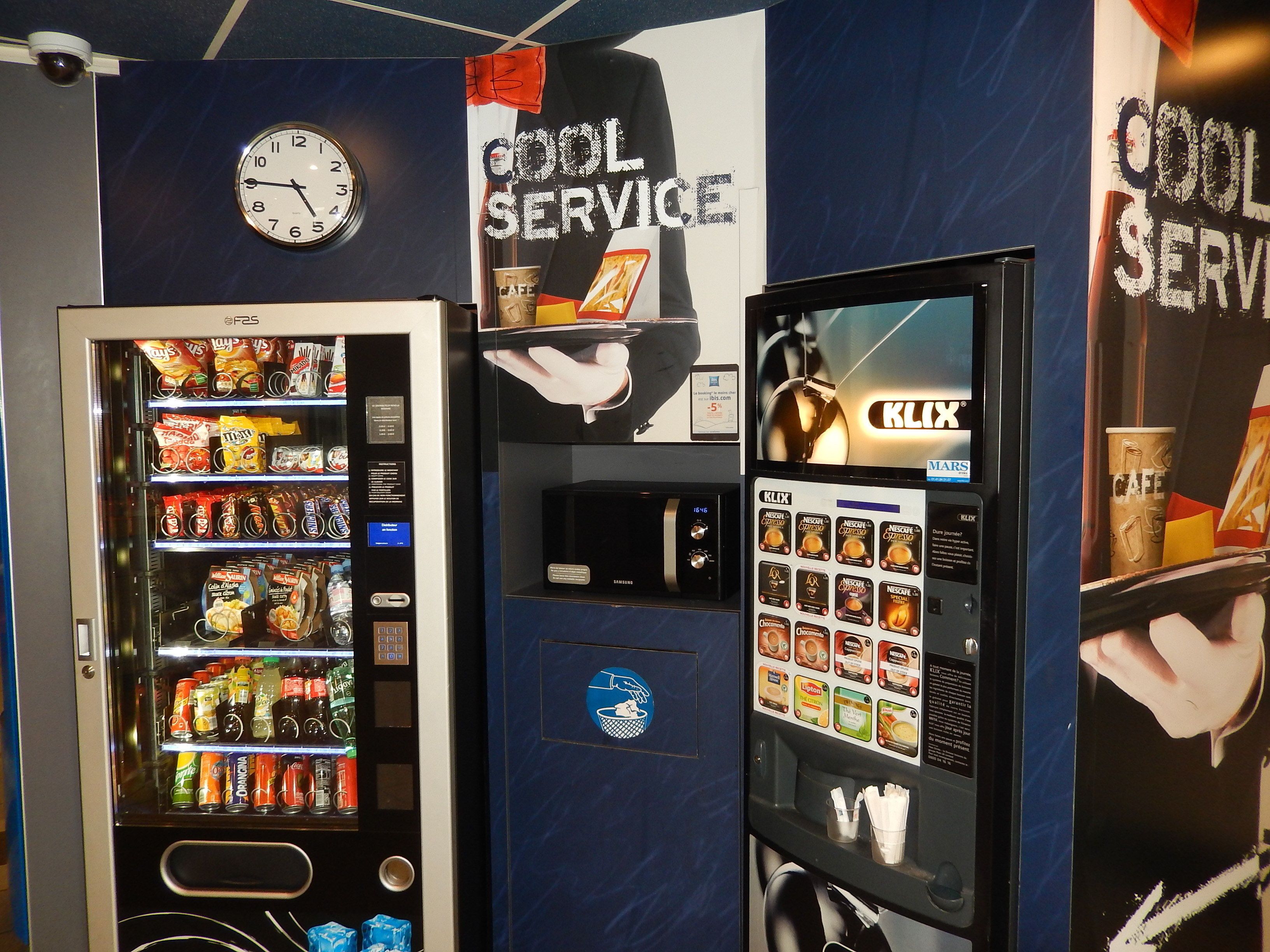 A vending machine area with a clock, a 'Cool Service' sign, and a K-LIX coffee machine.