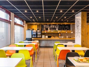 Un café avec des chaises aux couleurs vives, un comptoir où sont exposés des produits alimentaires et un plafond orné d’un motif en losanges.